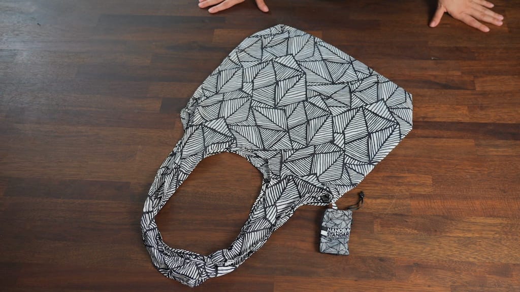 Black and white patterned foldable travel tote bag on a wooden surface.