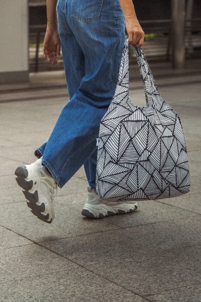 black and white geometric patterned foldable travel tote bag held by a person walking
