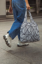 black and white geometric patterned foldable travel tote bag held by a person walking